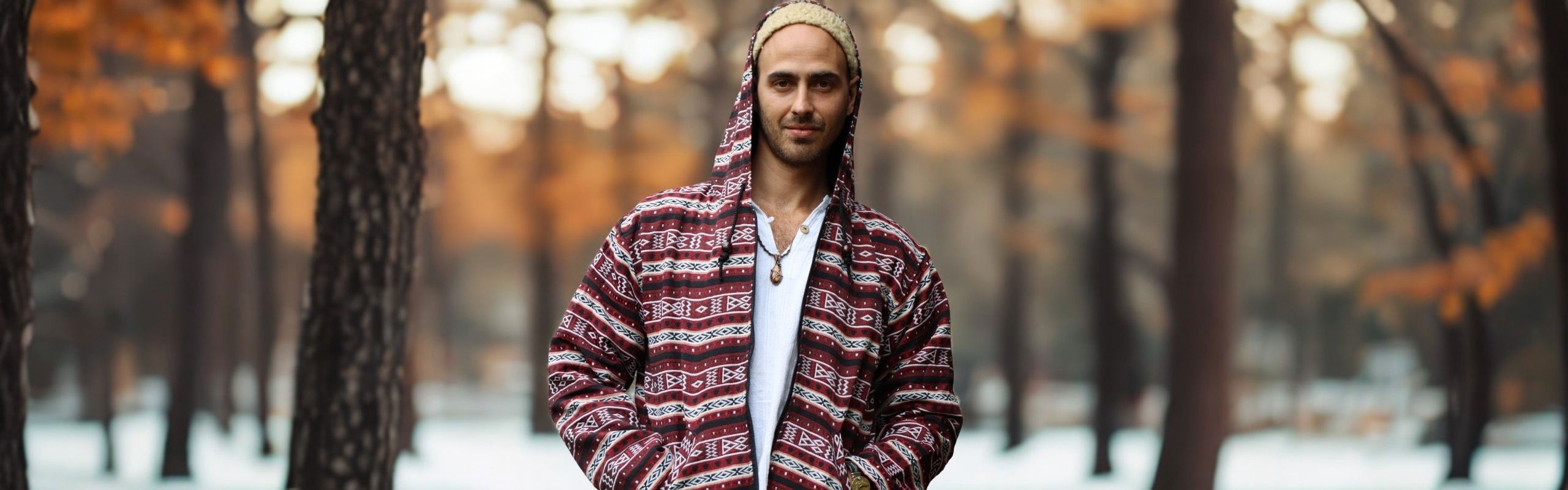 Mann trägt eine rote Herren Hoodie-Jacke mit Ethno-Muster und weißem Shirt in einem herbstlichen Wald
