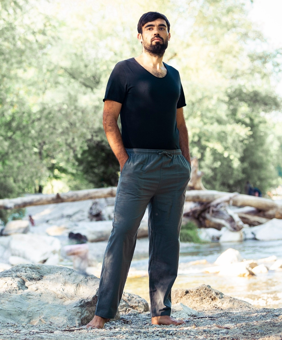 Mann trägt eine graue Herren-Loungehose mit schwarzem T-Shirt und steht barfuß am Flussufer