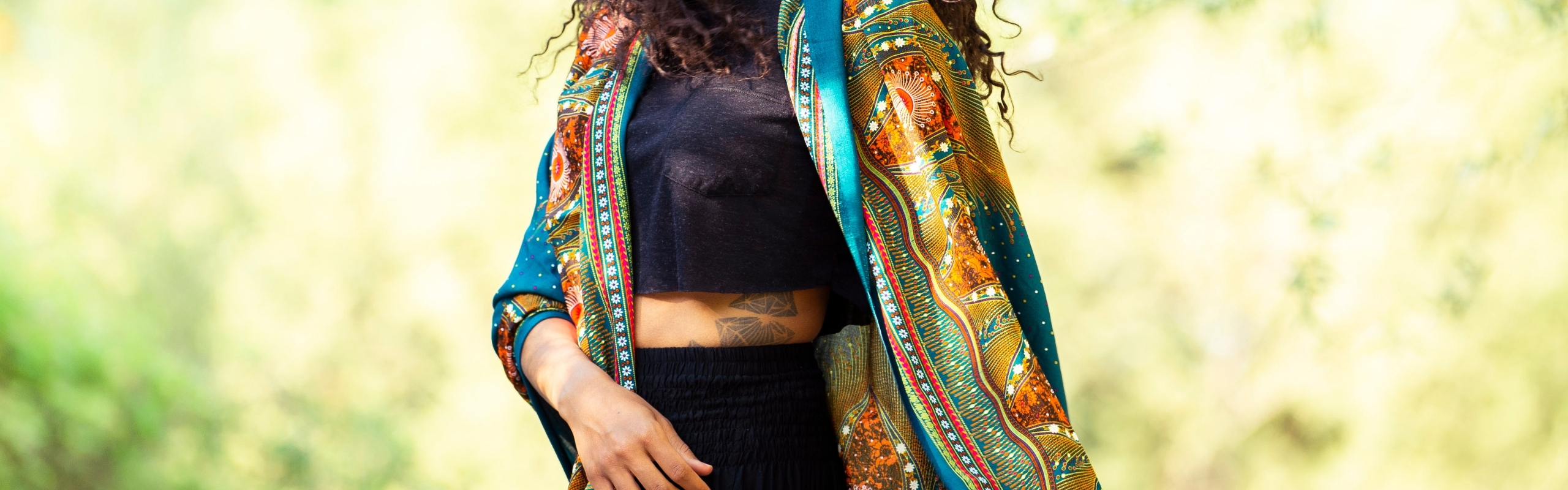 Model trägt einen gemusterten Damen-Kimono in Türkis und Orange über schwarzem Crop-Top und schwarzer Hose