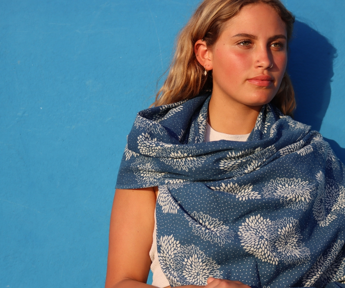 Woman wearing a blue women’s scarf with white floral pattern against a blue background