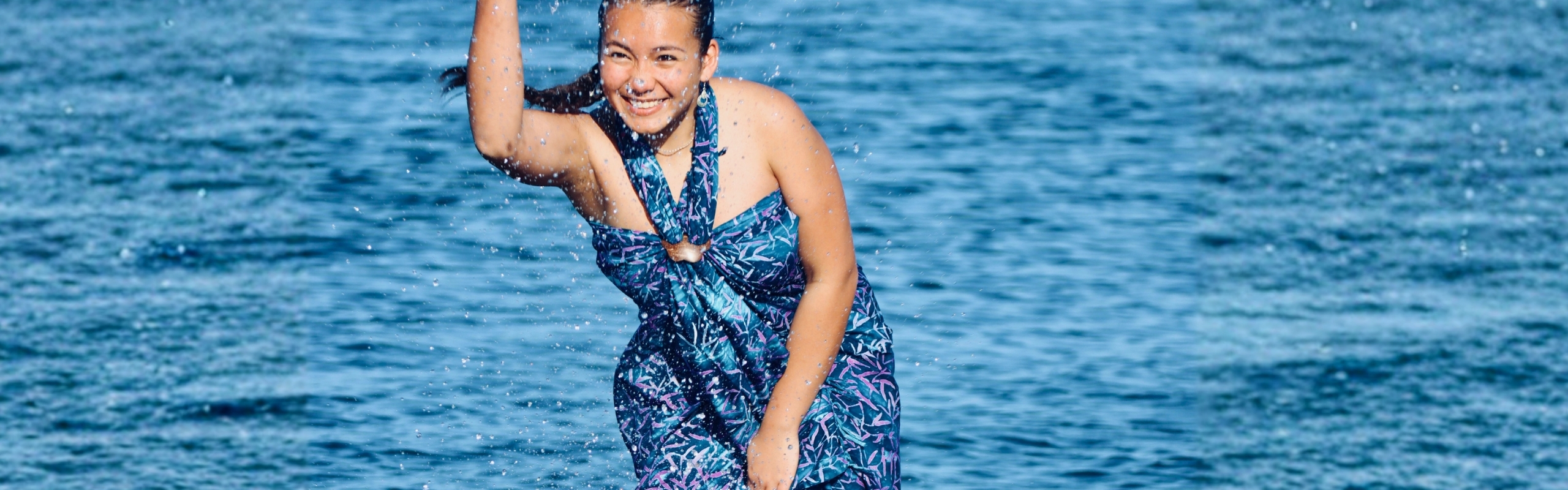 Lächelnde Frau im Wasser mit blauem Damen-Badeanzug mit tropischem Muster und Ringdetail