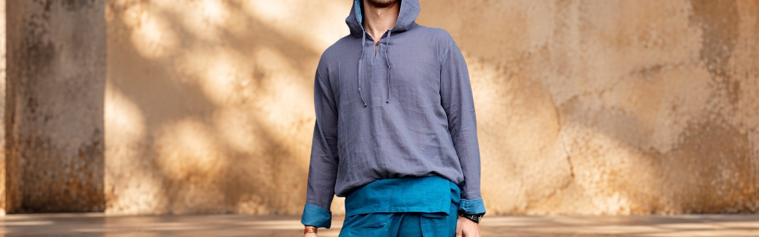 Mann trägt einen blauen Herren-Hoodie aus leichter Baumwolle mit Kapuze und langen Ärmeln vor heller Steinwand