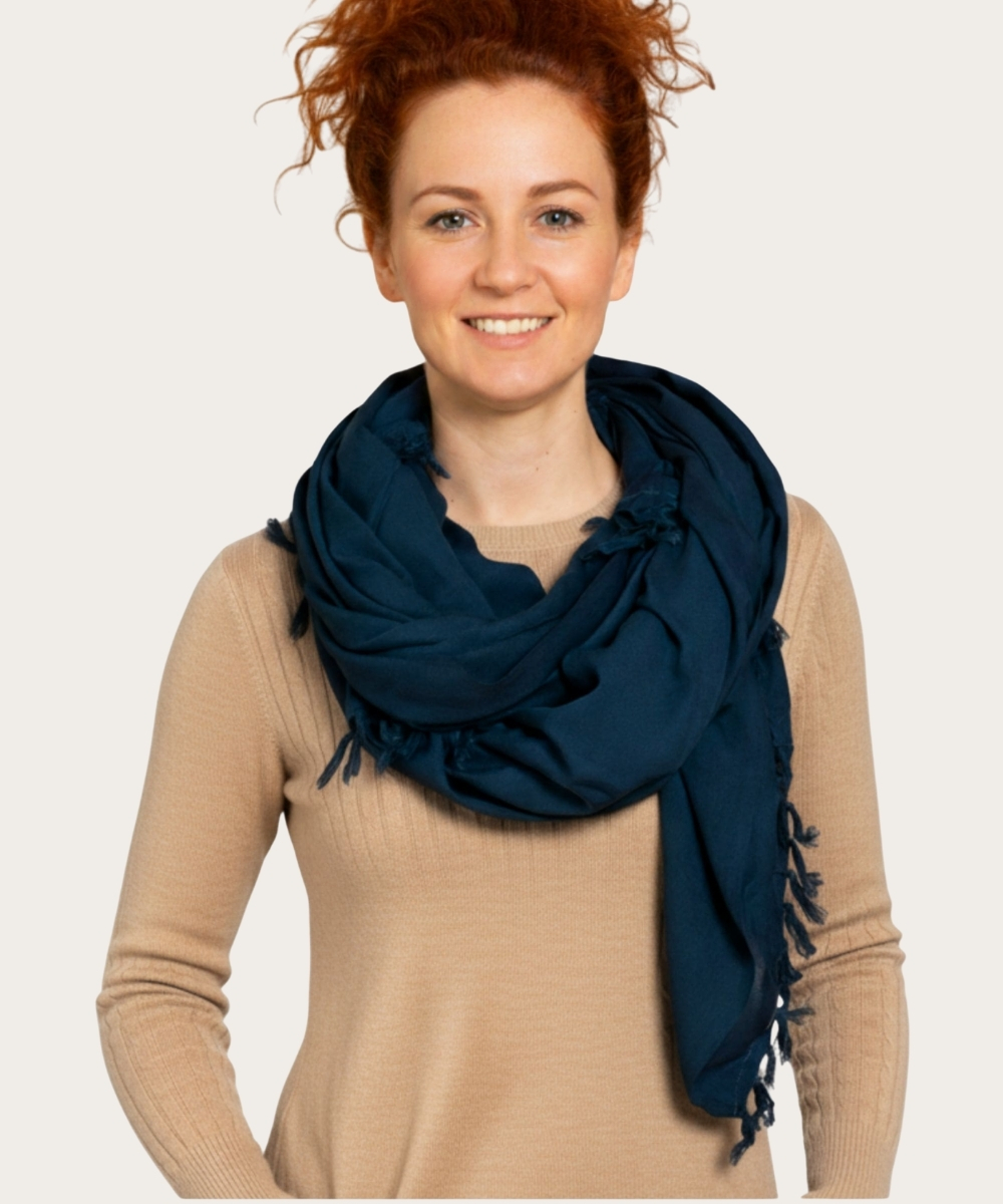 Frau mit dunkelblauem Schal mit Fransen und beigem Pullover, frontal vor hellem Hintergrund