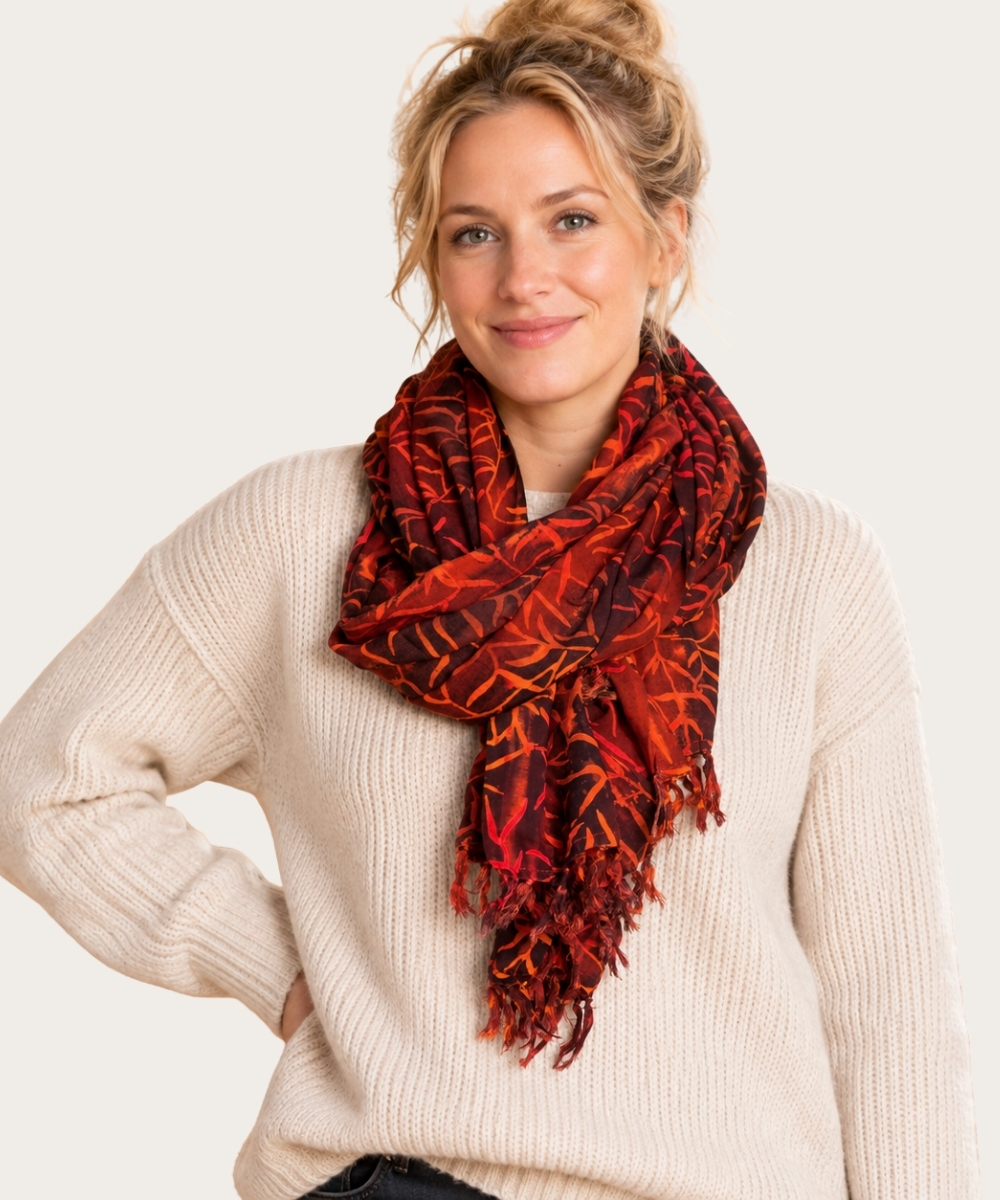 Model trägt einen rot-orangen Damenschal mit grafischem Muster und Fransen zu einem cremefarbenen Strickpullover