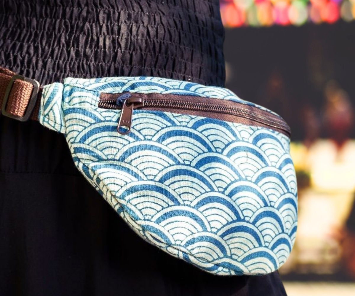 Person wearing a bum bag with a blue and white wave pattern, brown strap and zip fastening at the waist
