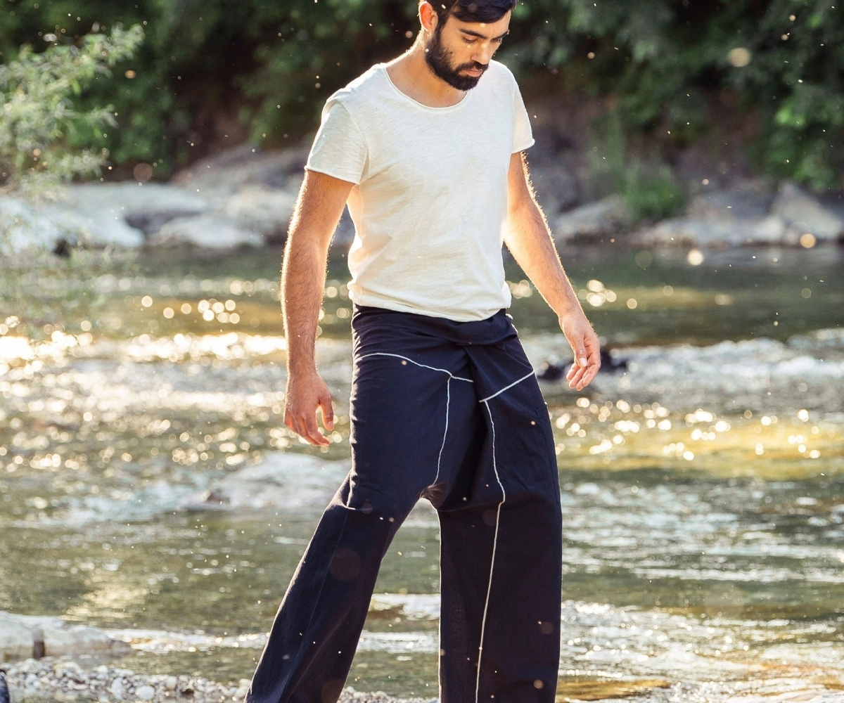 Mann trägt eine dunkelblaue Herrenhose mit Kontrastnähten und weißem T-Shirt bei einem Spaziergang am Fluss