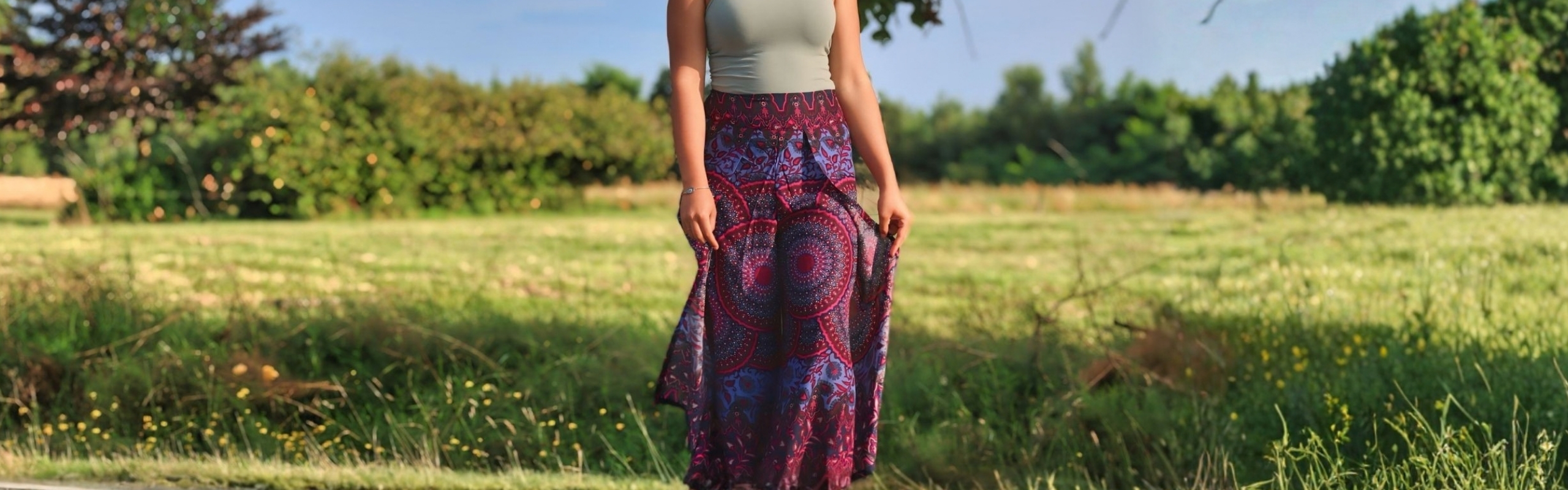 Model trägt einen langen Boho-Rock mit ornamentalem Muster in Violett und Rot auf einer Wiese im Freien