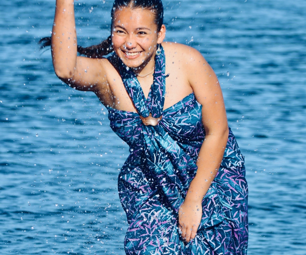 Frau im blauen Badeanzug mit tropischem Muster steht lächelnd im Wasser