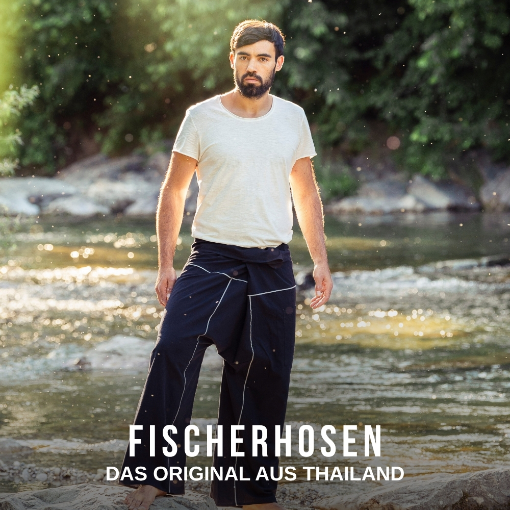 Mann trägt eine dunkelblaue Fischerhose aus Thailand mit weißem T-Shirt am Flussufer