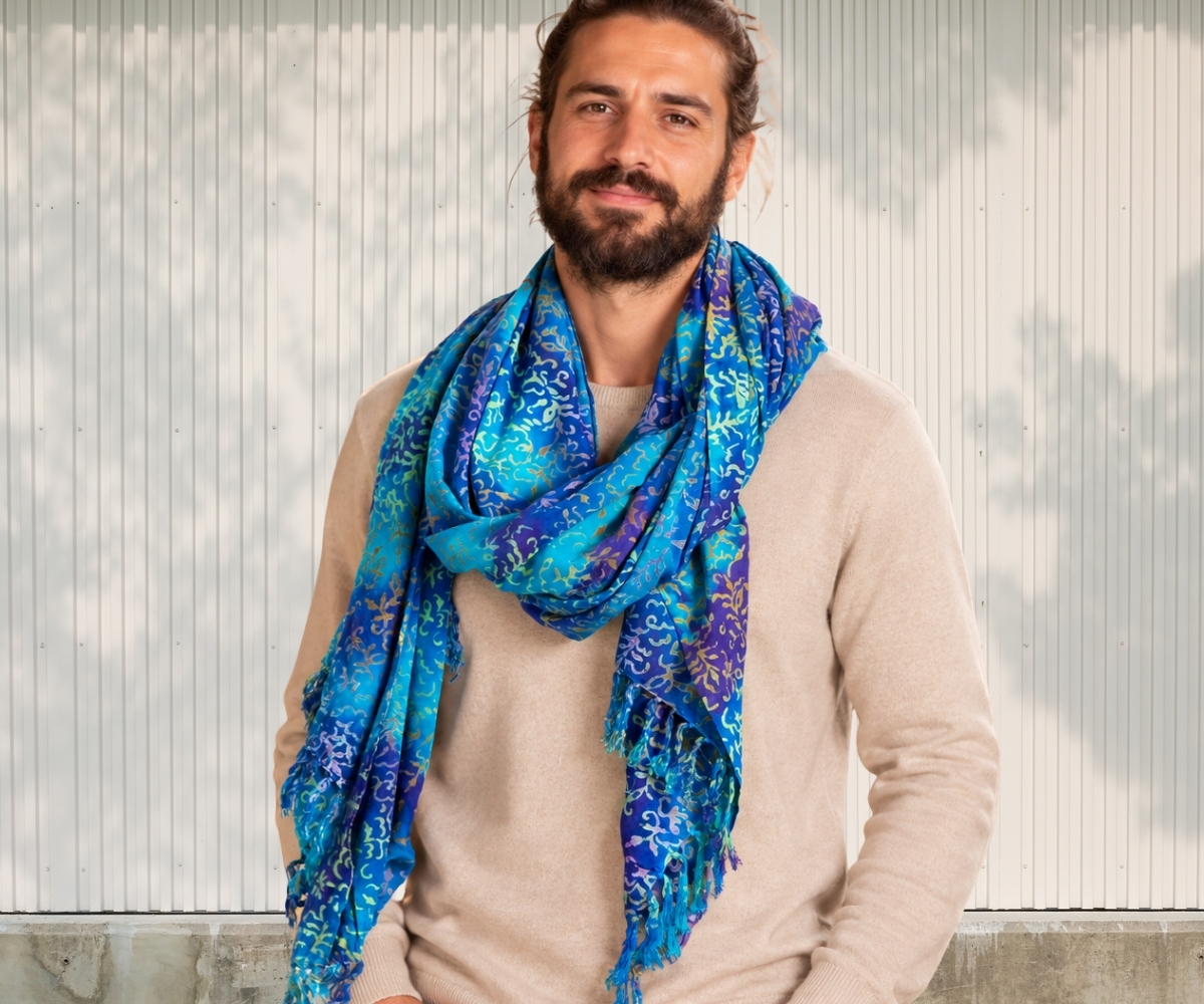 Mann trägt einen großen blau-türkisen Schal mit Muster zu beigem Pullover