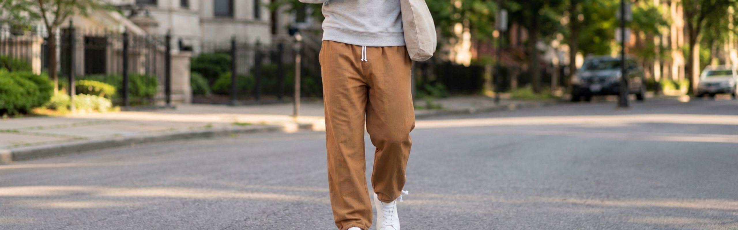 Model trägt eine braune Herren-Jogginghose mit Kordelzug und weißen Sneakern auf einer Stadtstraße