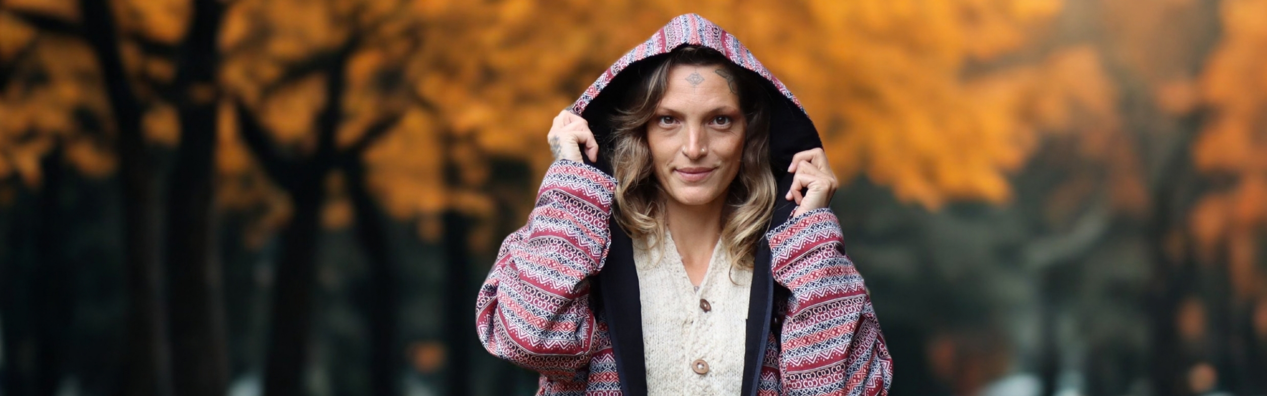 Frau trägt eine gemusterte Damen Hoodie-Jacke mit Kapuze vor unscharfem Herbstwald