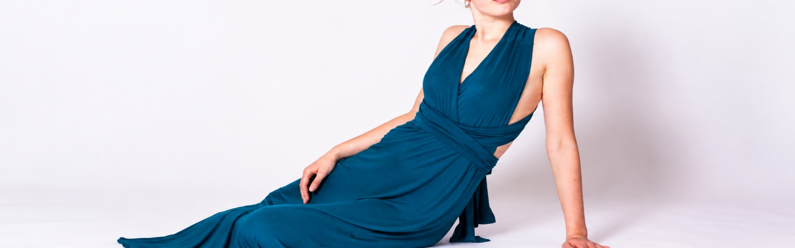 Model wearing a floor-length petrol evening dress with a deep V-neckline, wrap design and open back.