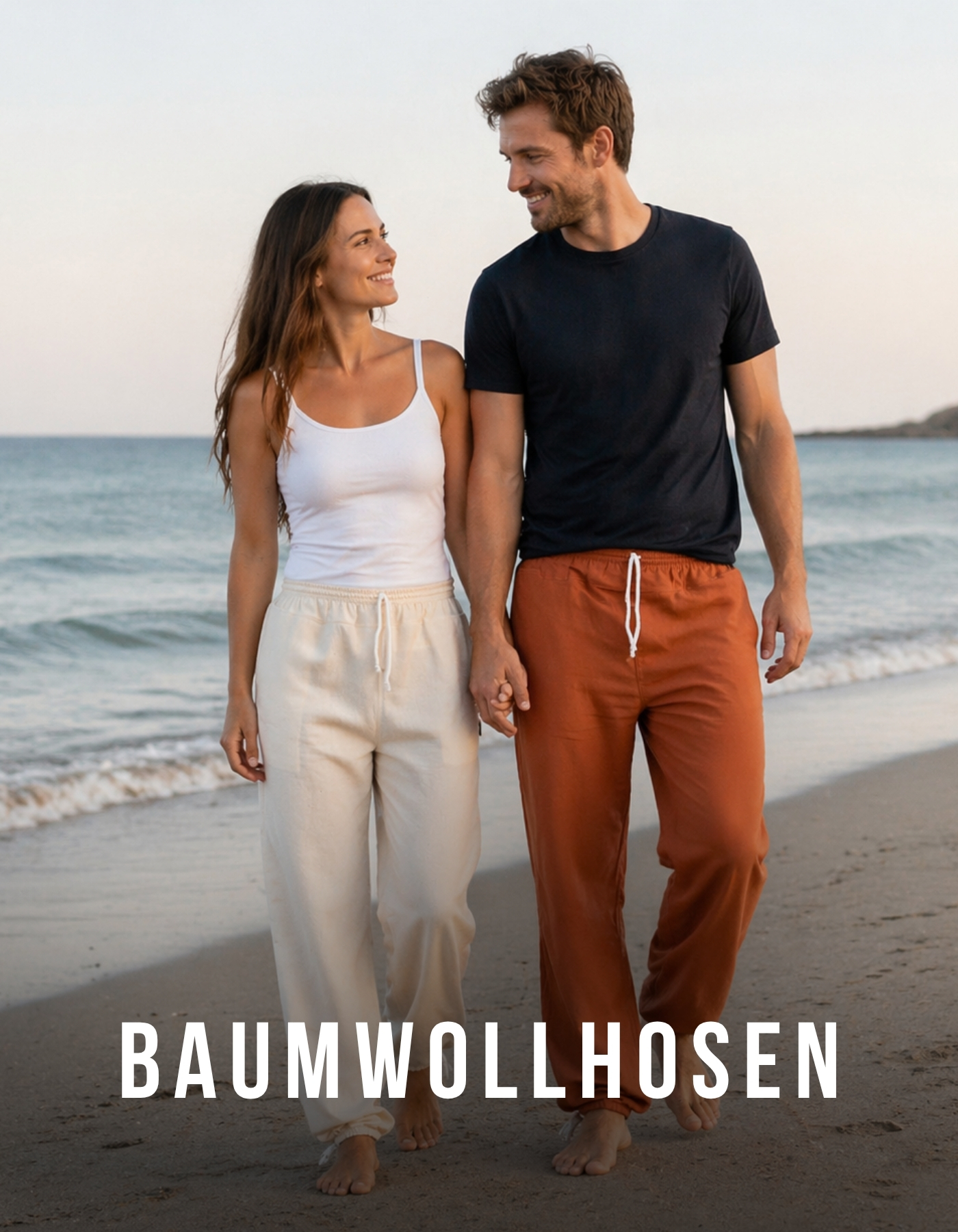 Dame und Herr tragen leichte Baumwollhosen und spazieren barfuß Hand in Hand am Strand