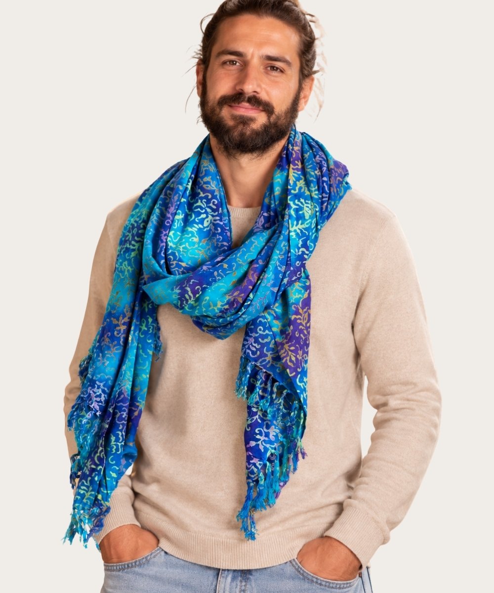 Mann trägt einen blau-türkisen Schal mit ornamentalem Muster und Fransen zu beigem Pullover