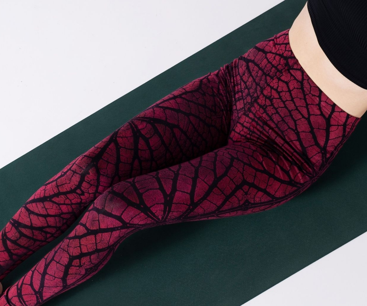 Model wearing fitted women’s fitness leggings in burgundy with a black marble pattern on a yoga mat