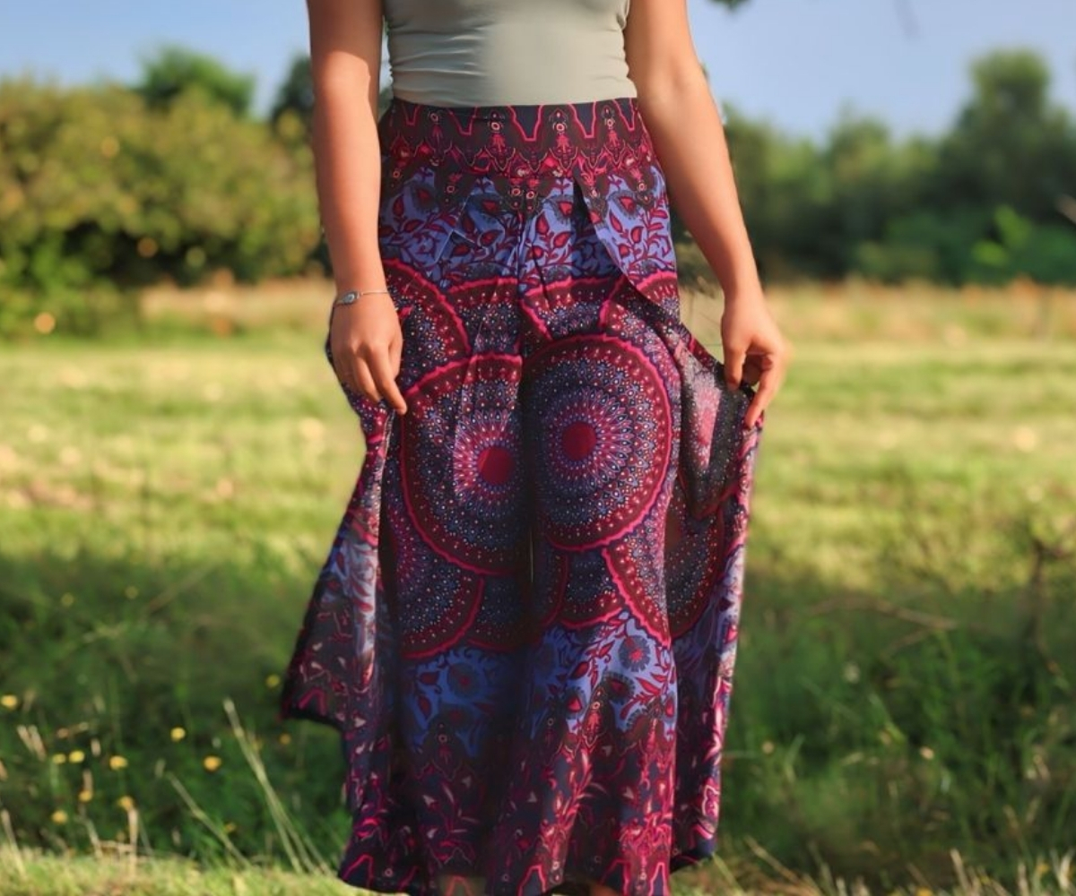 Model trägt einen langen, fließenden Boho-Rock mit Mandala-Print in Lila, Pink und Blau auf einer Wiese