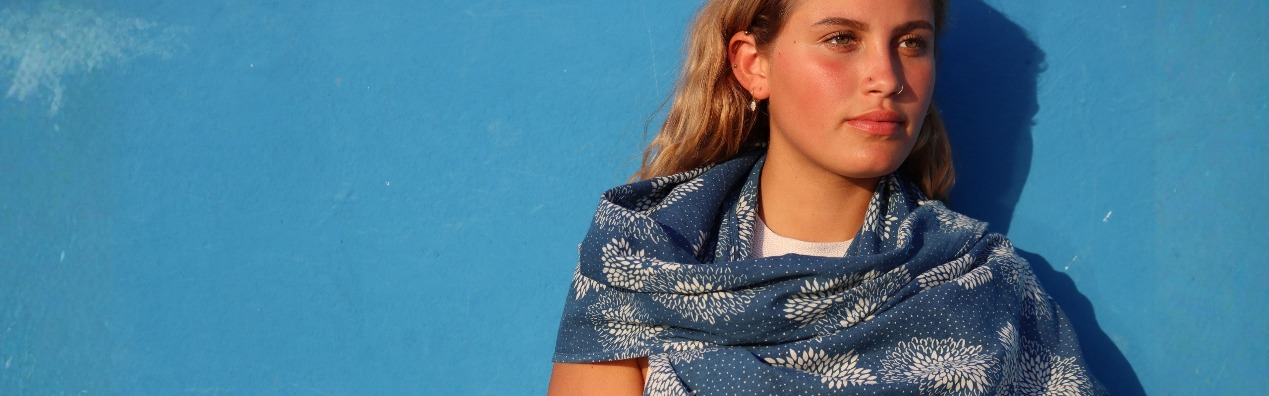 Woman wearing a blue women’s scarf with white floral pattern against a blue background