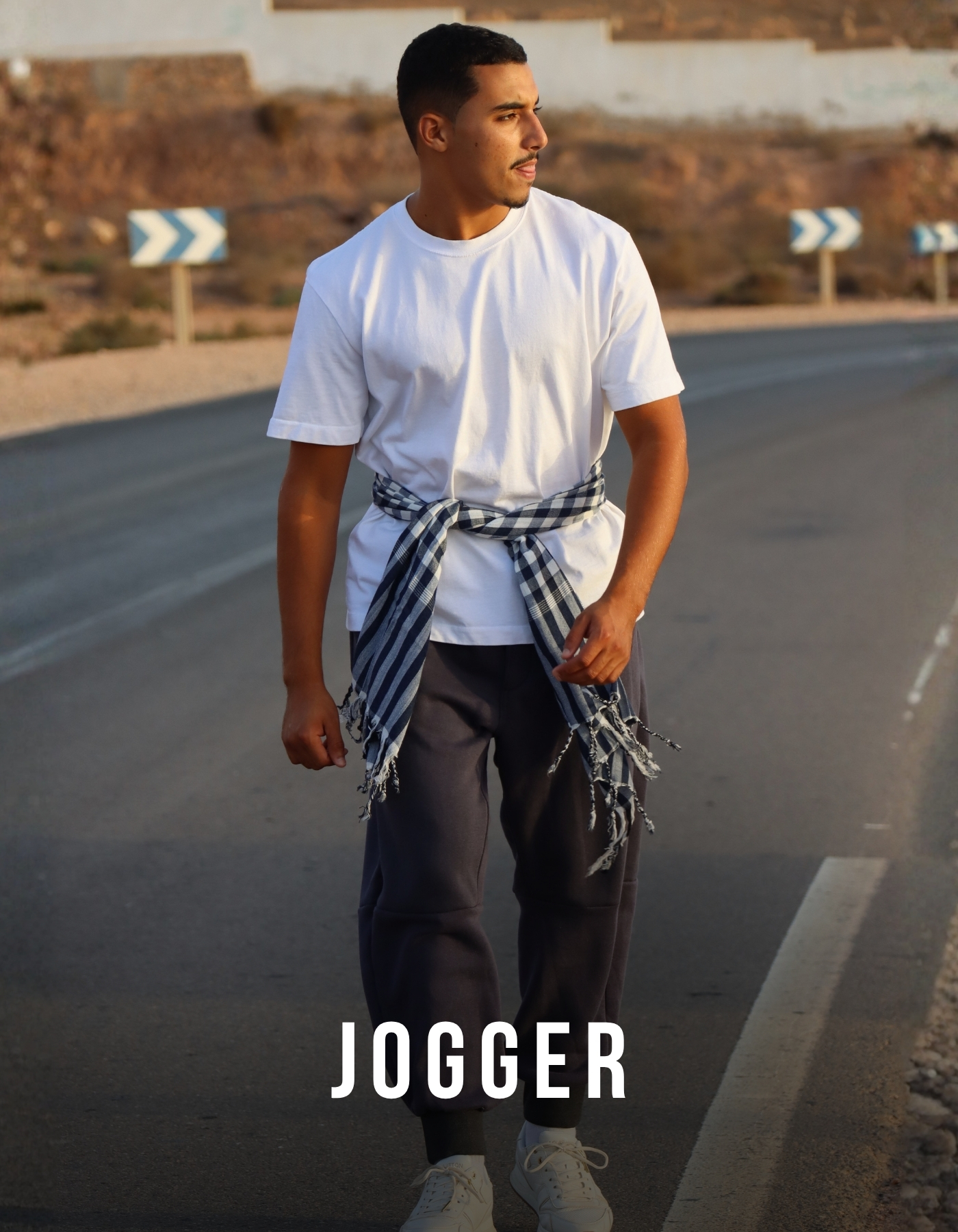 Model trägt dunkelblaue Herren-Jogger mit weißem T-Shirt und Sneakern auf einer Straße im Casual-Look